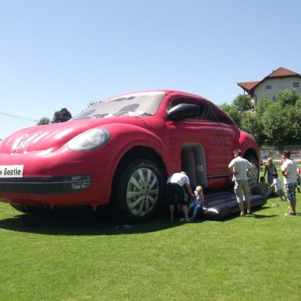 Hüpfburg VW Beetle in rot auf Wiese aufgebaut mit Kindern und Erwachsenen davor
